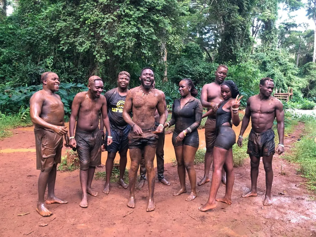 A group of mud-covered trip members smiling after a mud run in the forest