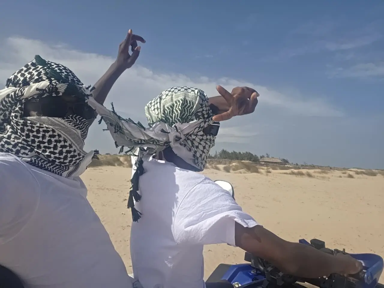 Riders in headwraps on a quad bike crossing coastal sand dunes
